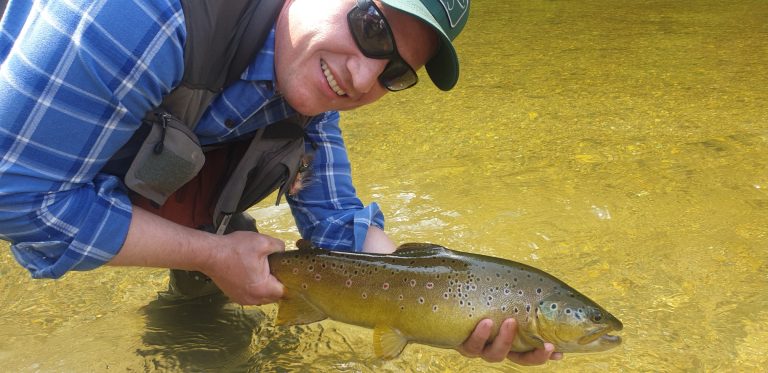Angler kniet im Wasser und hält lachend eine Bachforelle der bayerischen Traun